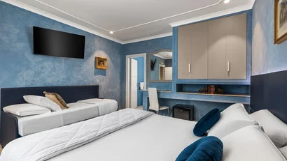 Camera d'hotel con letto matrimoniale, letto singolo, TV a muro e pareti blu