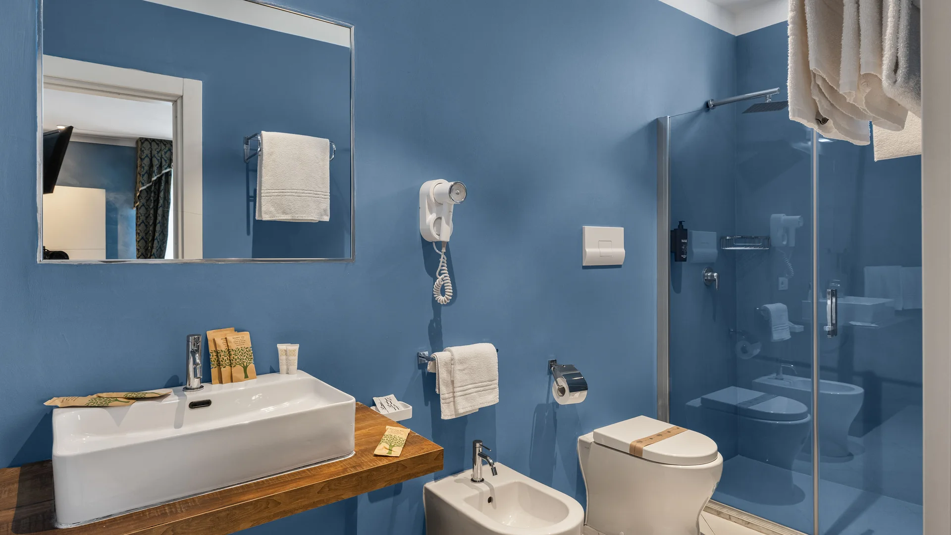 Bagno moderno con pareti blu, lavabo, bidet, WC e doccia con parete in vetro
