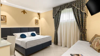 Camera d'albergo con letto matrimoniale, divano, tende ornate e TV a parete