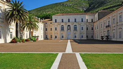 Cortile con edificio storico bianco e palme davanti a una montagna verde