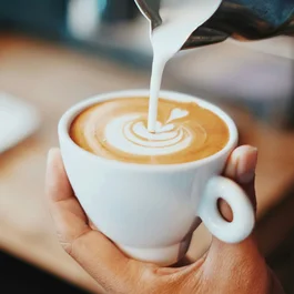 mano che tiene una tazza bianca mentre si versa latte nel caffè con arte latte