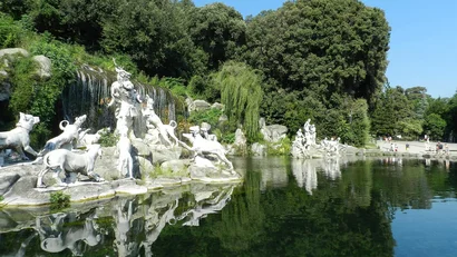 Statue di cani e figure umane vicino a una cascata e un lago con riflessi
