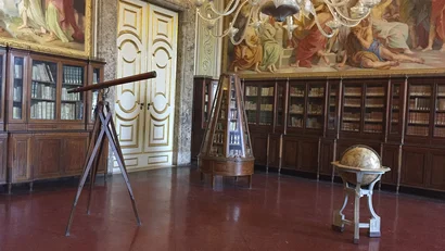 Sala storica con telescopio, globo e librerie in legno con affreschi alle pareti