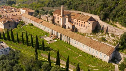 Veduta aerea di un edificio storico con tetti in tegole e alberi cipressi