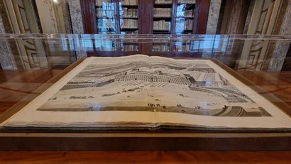 Libro antico aperto con illustrazione di un palazzo storico in una teca di vetro